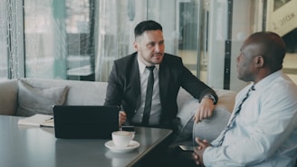 Two businessmen talking at a table with laptop.