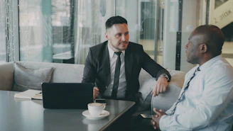 Two businessmen talking at a table with laptop.