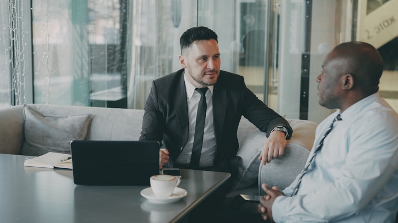 Two businessmen talking at a table with laptop.