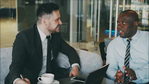 Two businessmen in suits talking at a table.
