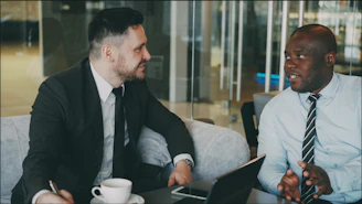 Two businessmen in suits talking at a table.