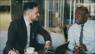 Two businessmen in suits talking at a table.