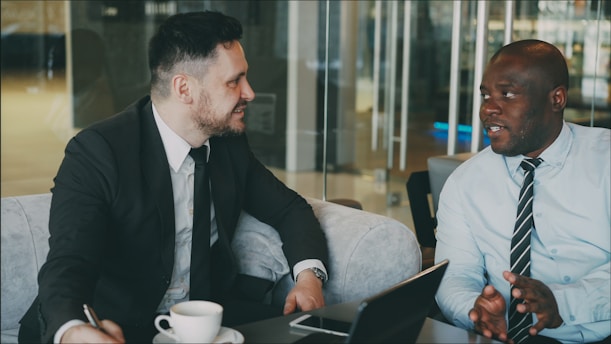 Two businessmen in suits talking at a table.