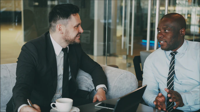 Two businessmen in suits talking at a table.
