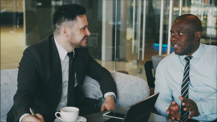 Two businessmen in suits talking at a table.