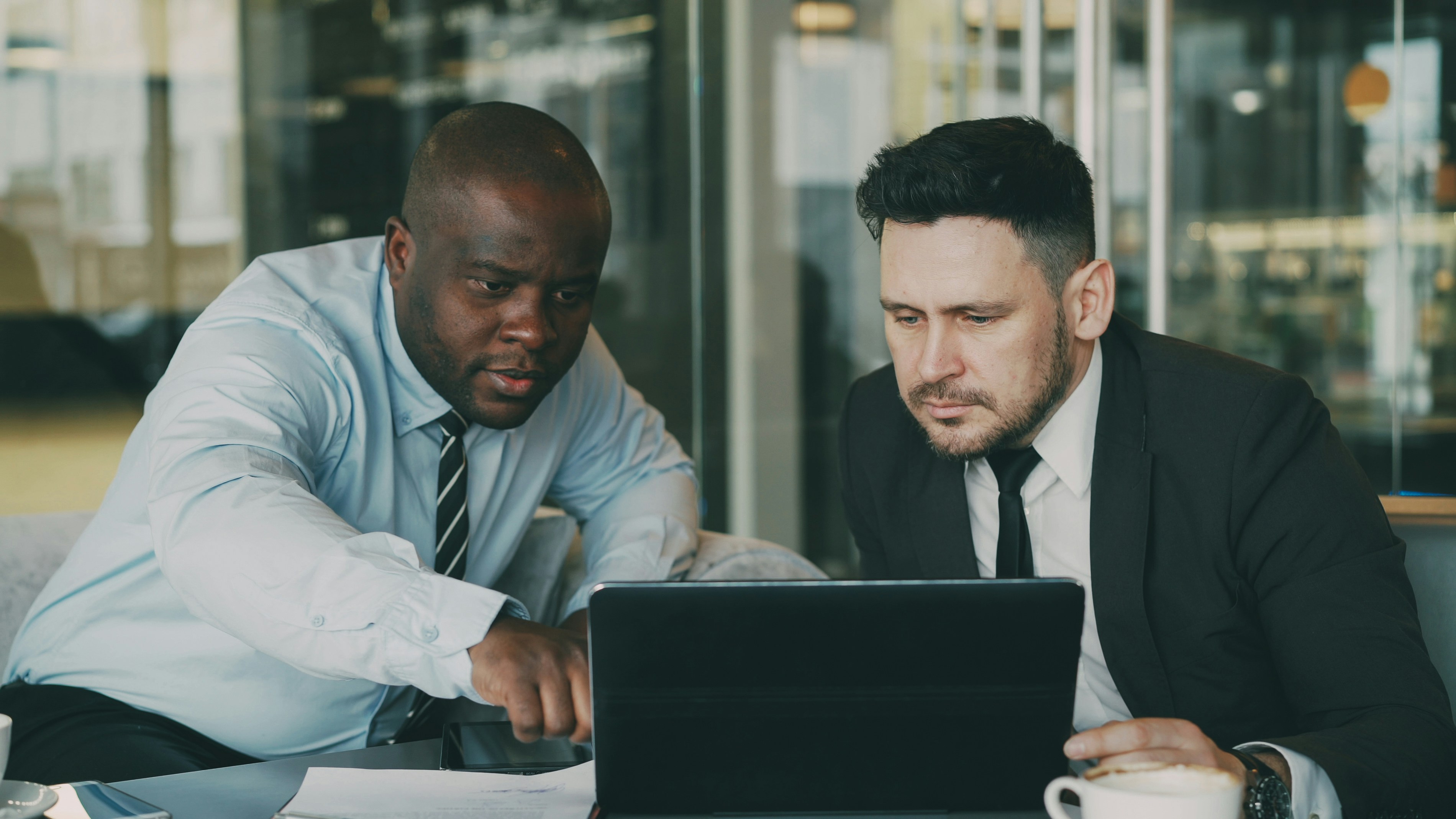 Two business colleagues looking at laptop computer and discussing their startup plan in modern office with glass walls