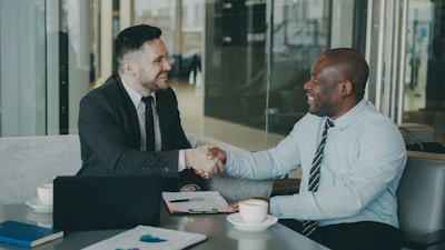 Two businessmen shaking hands across a table.