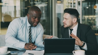 Two businessmen collaborating over a tablet and laptop.