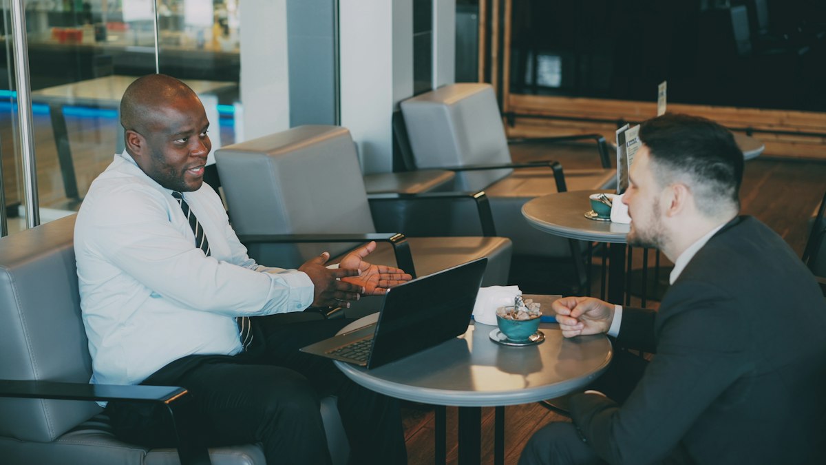 Two professionals in conversation at a cafe table with a laptop