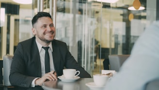 Two men in suits having coffee at a table.