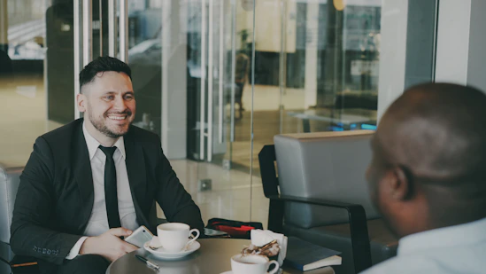 Two businessmen smiling and talking at a cafe table.