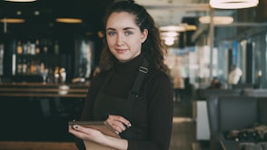 Woman in apron holding tablet in restaurant
