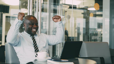 Man celebrating success in office with laptop.