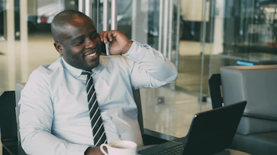 Man talking on phone with coffee and laptop.