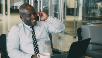 Man talking on phone with coffee and laptop.