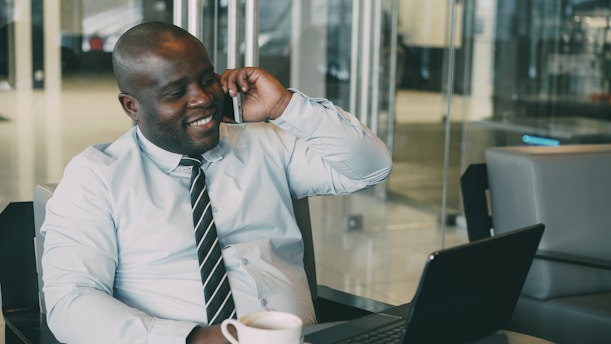 Man talking on phone with coffee and laptop.