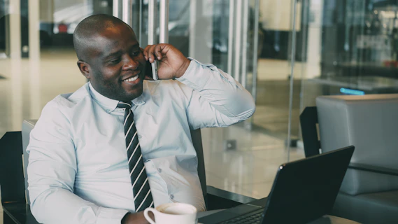 Man talking on phone with coffee and laptop.