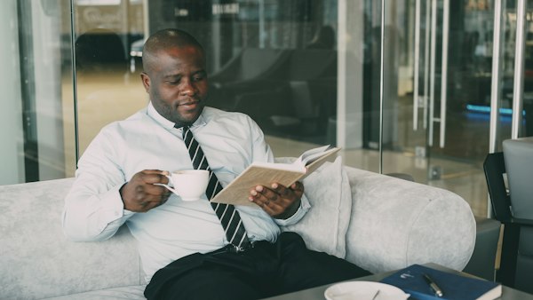 Man in shirt and tie reading a book with coffee