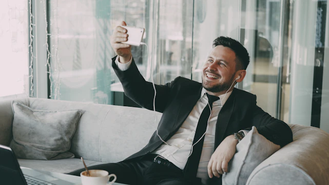 Man in suit taking a selfie on a couch.