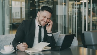 Man in suit talking on phone while writing.