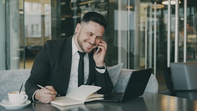 Man in suit talking on phone while writing.