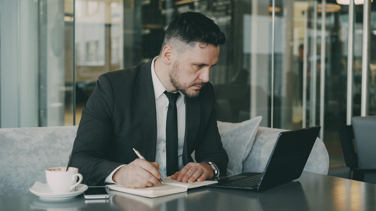 Dirigeant de PME qui cadre sa cible commerciale au carnet, ordinateur portable ouvert sur la table