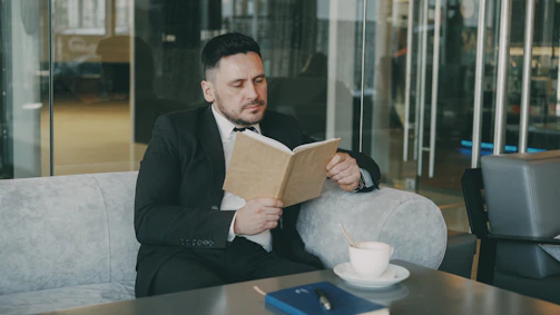 Man in suit reading a book with coffee.