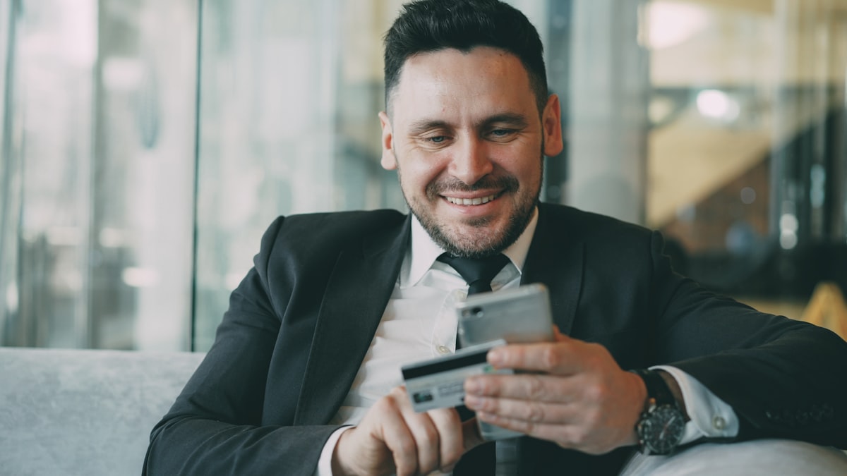 A man in a suit holds a smartphone and credit card, representing digital payment technology and fintech innovation