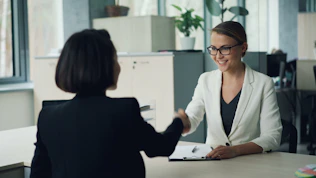 Two women shaking hands across a desk