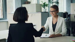Two women shaking hands across a desk