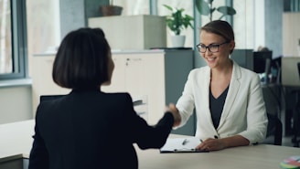 Two women shaking hands across a desk