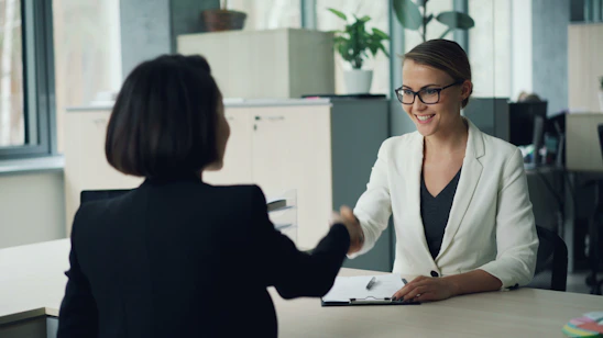 Two women shaking hands across a desk
