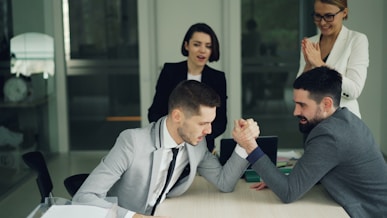Two businessmen arm wrestling while colleagues watch