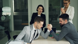Two businessmen arm wrestling while colleagues watch
