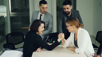 Two women arm wrestling with men watching them