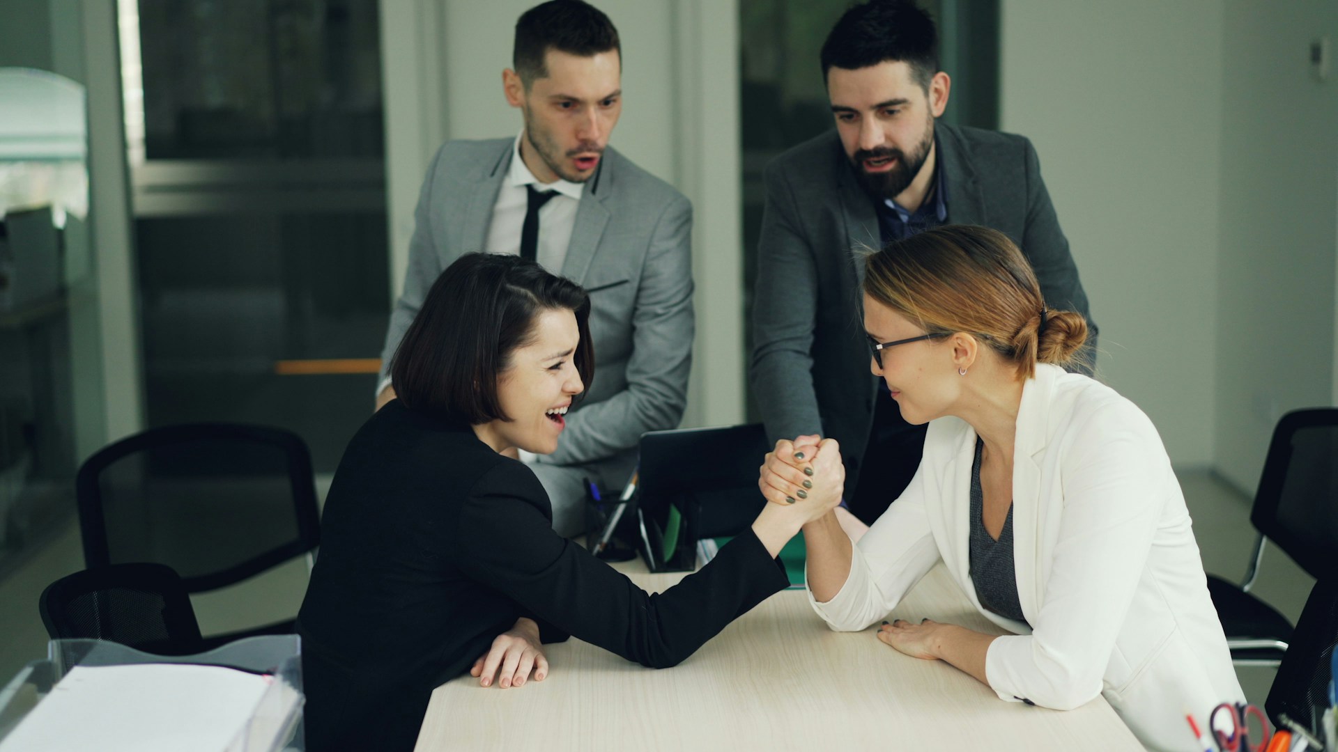 Two women arm wrestling with men watching them