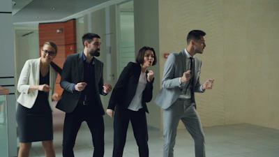 Four business people dancing in an office hallway.