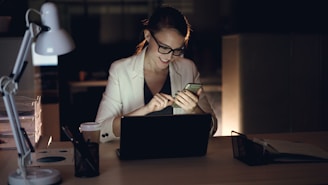 Woman working on phone and laptop at night