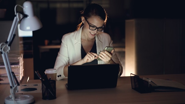 Woman working on phone and laptop at night