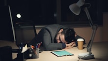 Man sleeping at desk with coffee and tablet.