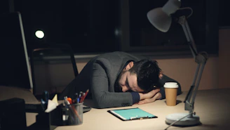 Man sleeping at desk with coffee and tablet.