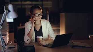 Woman talking on phone at desk with laptop and coffee.