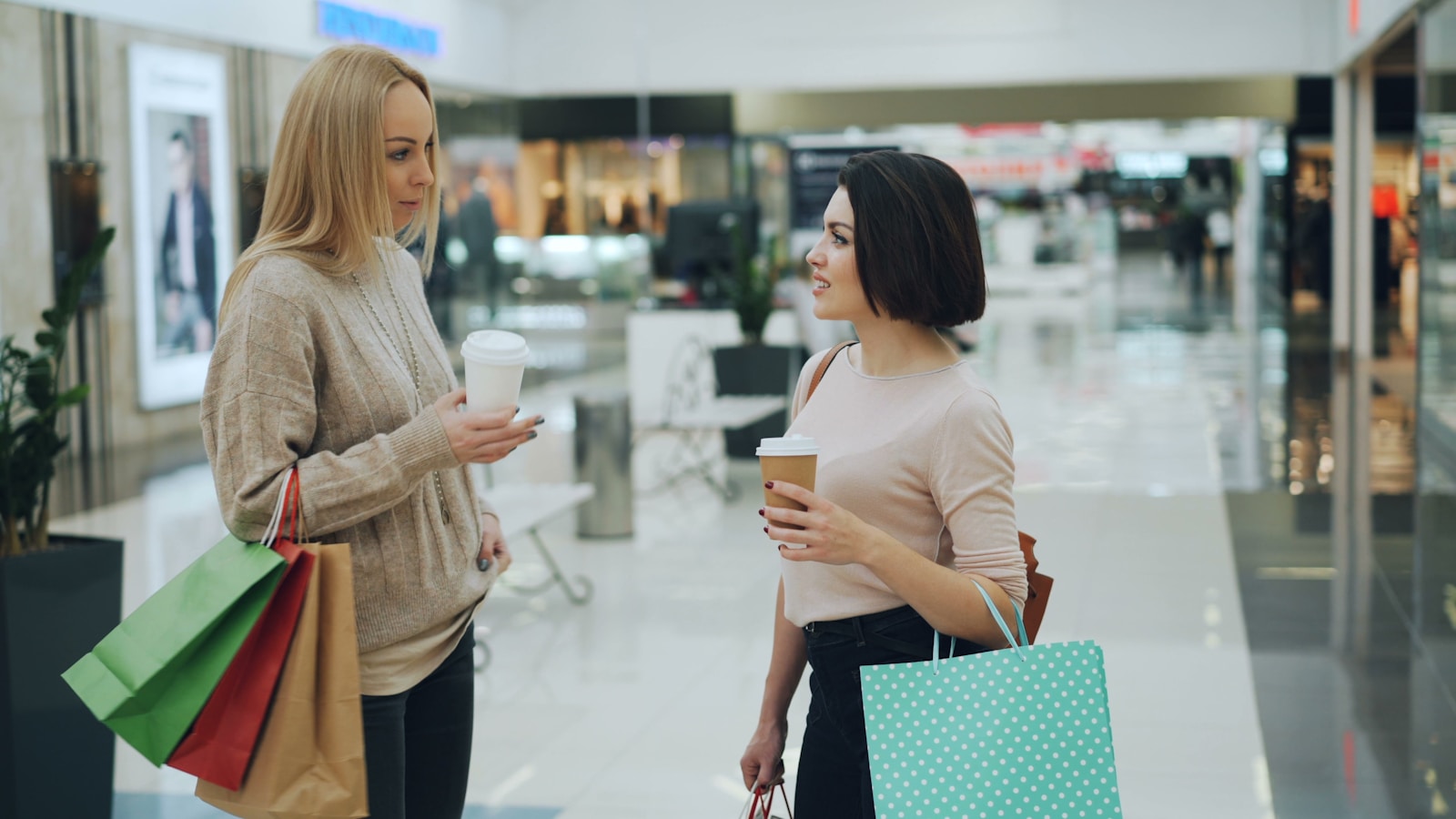 Two women talking while holding coffee and shopping bags.