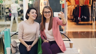 Two smiling women taking a selfie in a mall.