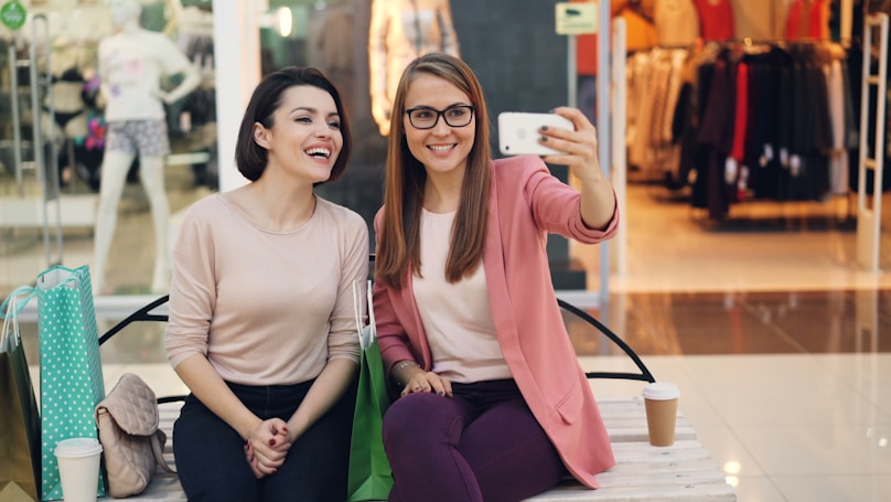 Two smiling women taking a selfie in a mall.