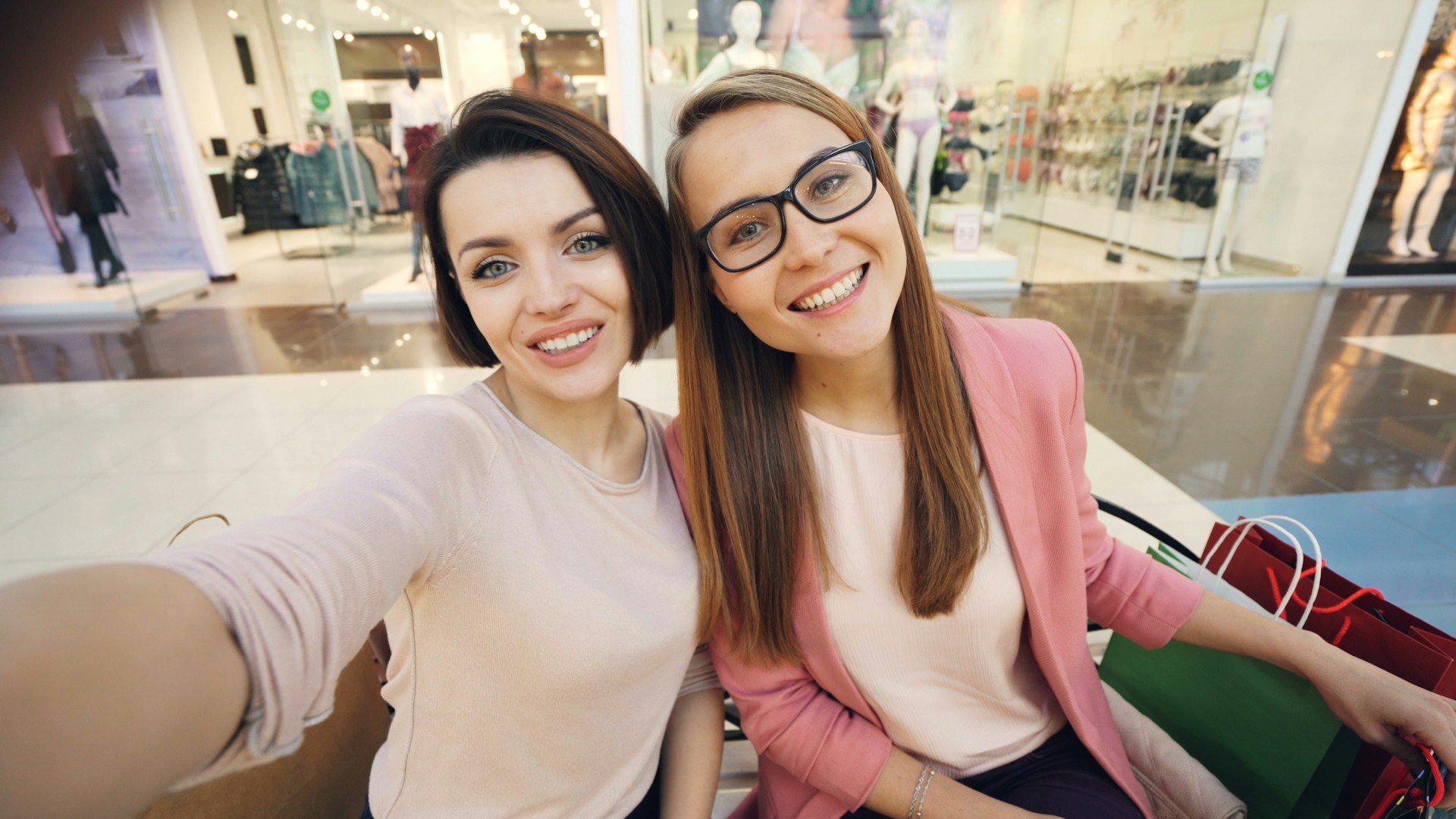 Two smiling women taking a selfie in a mall.