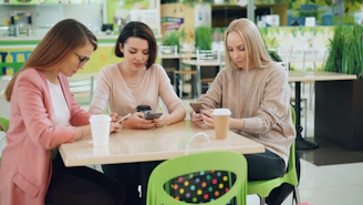 Three women looking at their phones at a cafe table.