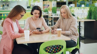 Three women looking at their phones at a cafe table.