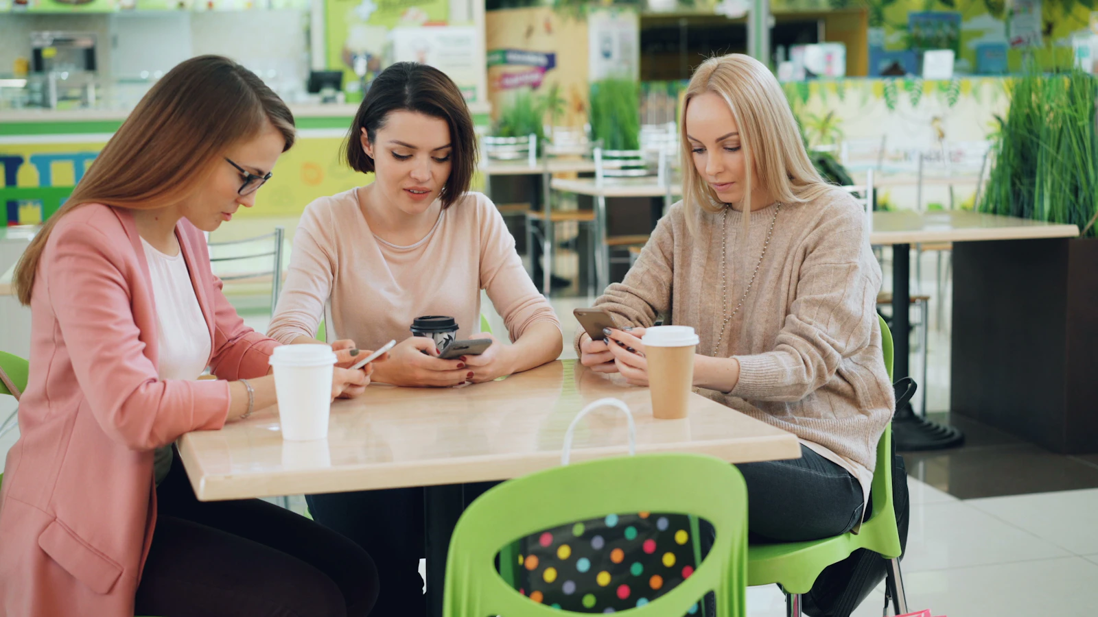 Tres personas revisando sus móviles en una cafetería