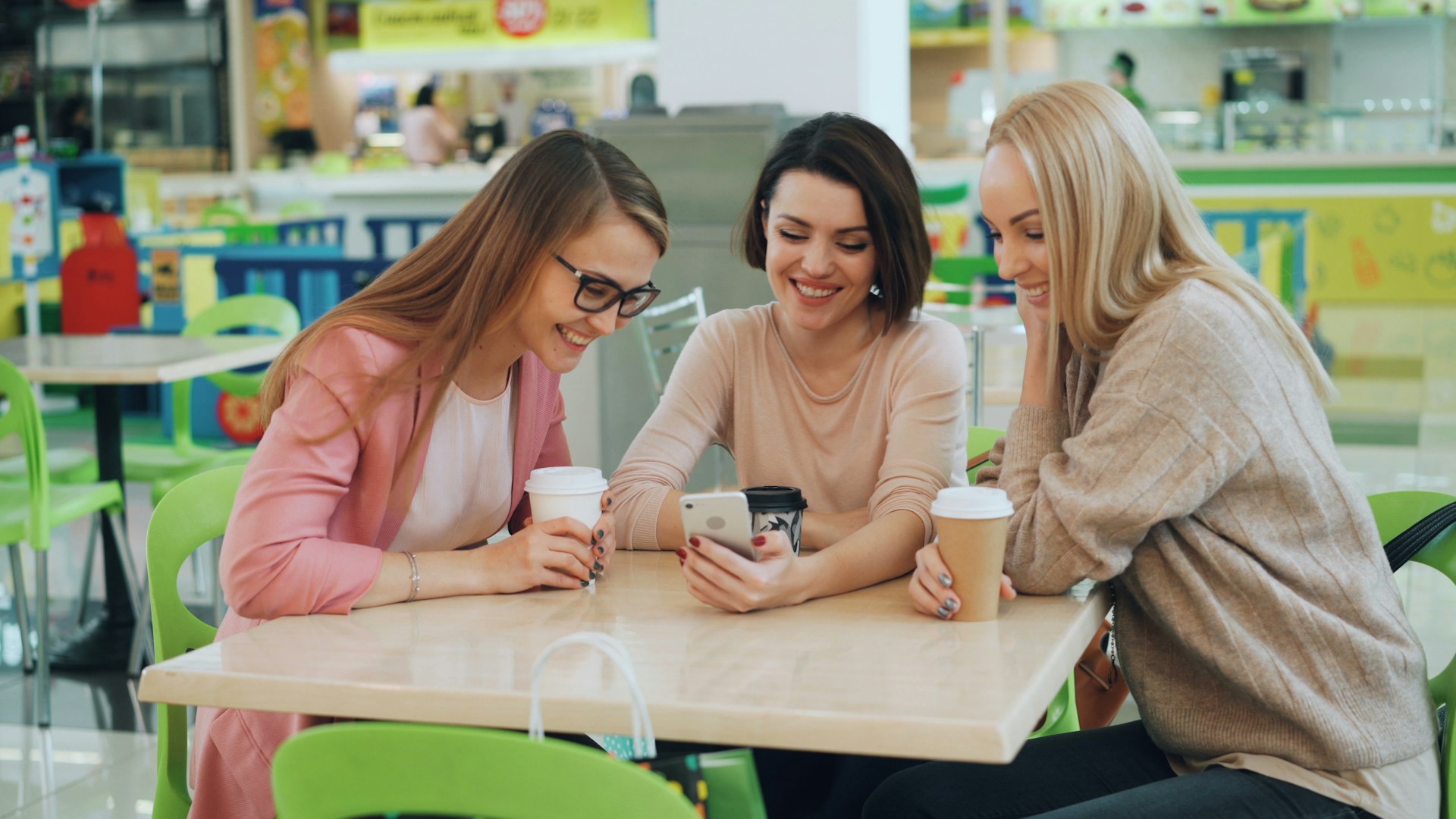 Three women looking at a smartphone at a cafe.